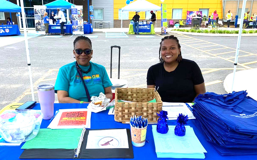 2 Goodwill employees under a tent sitting at table - Spring festival