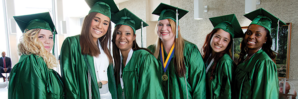 group of happy young adult women in green graduation caps and gowns 